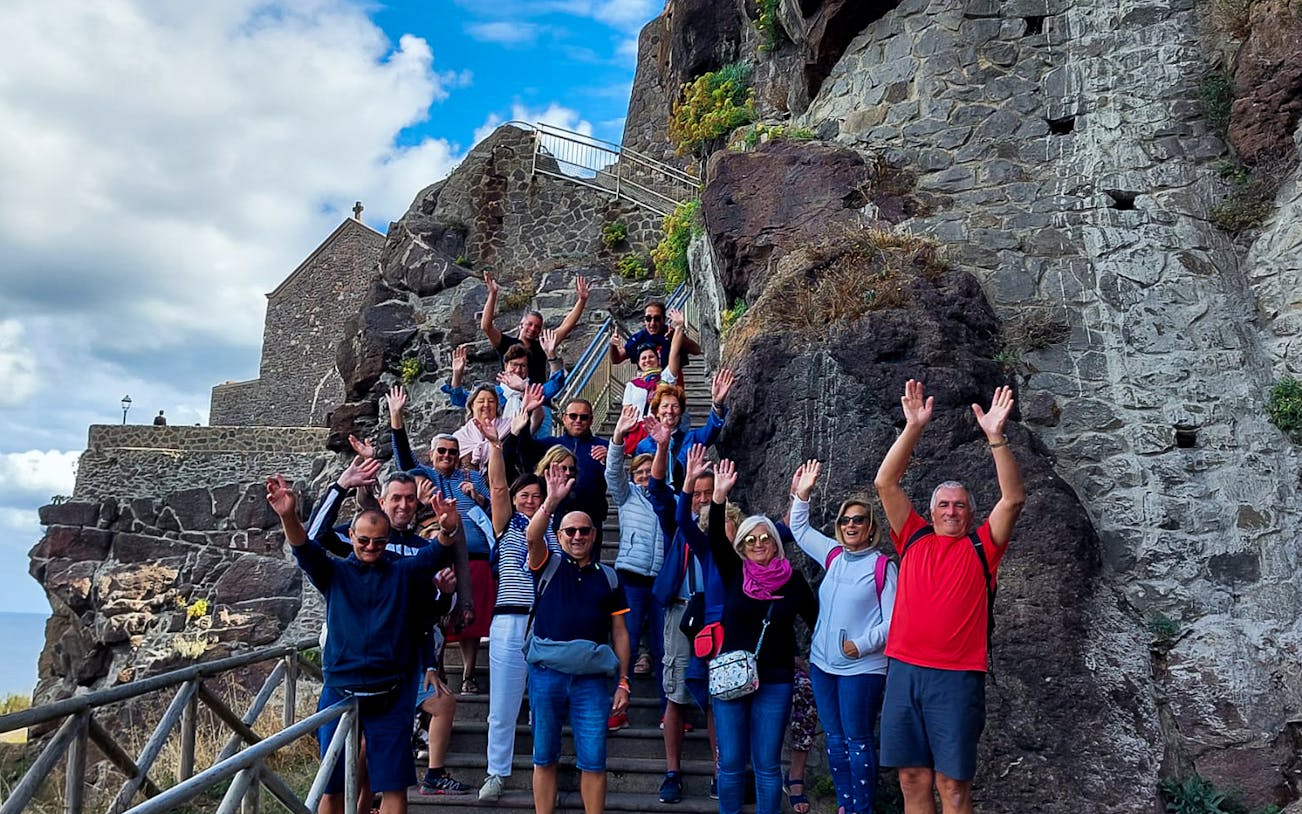 Group of tourists on a guided tour in Castelsardo, Sardinia, standing on stone steps.