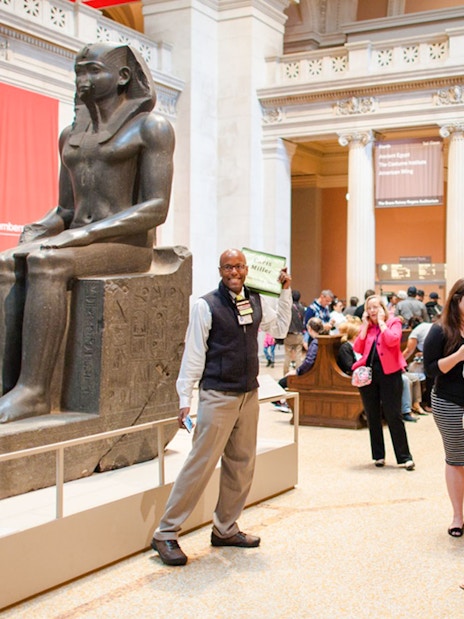 Guide engaging with tourists near ancient statue in Egyptian museum.