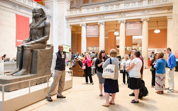 Guide engaging with tourists near ancient statue in Egyptian museum.