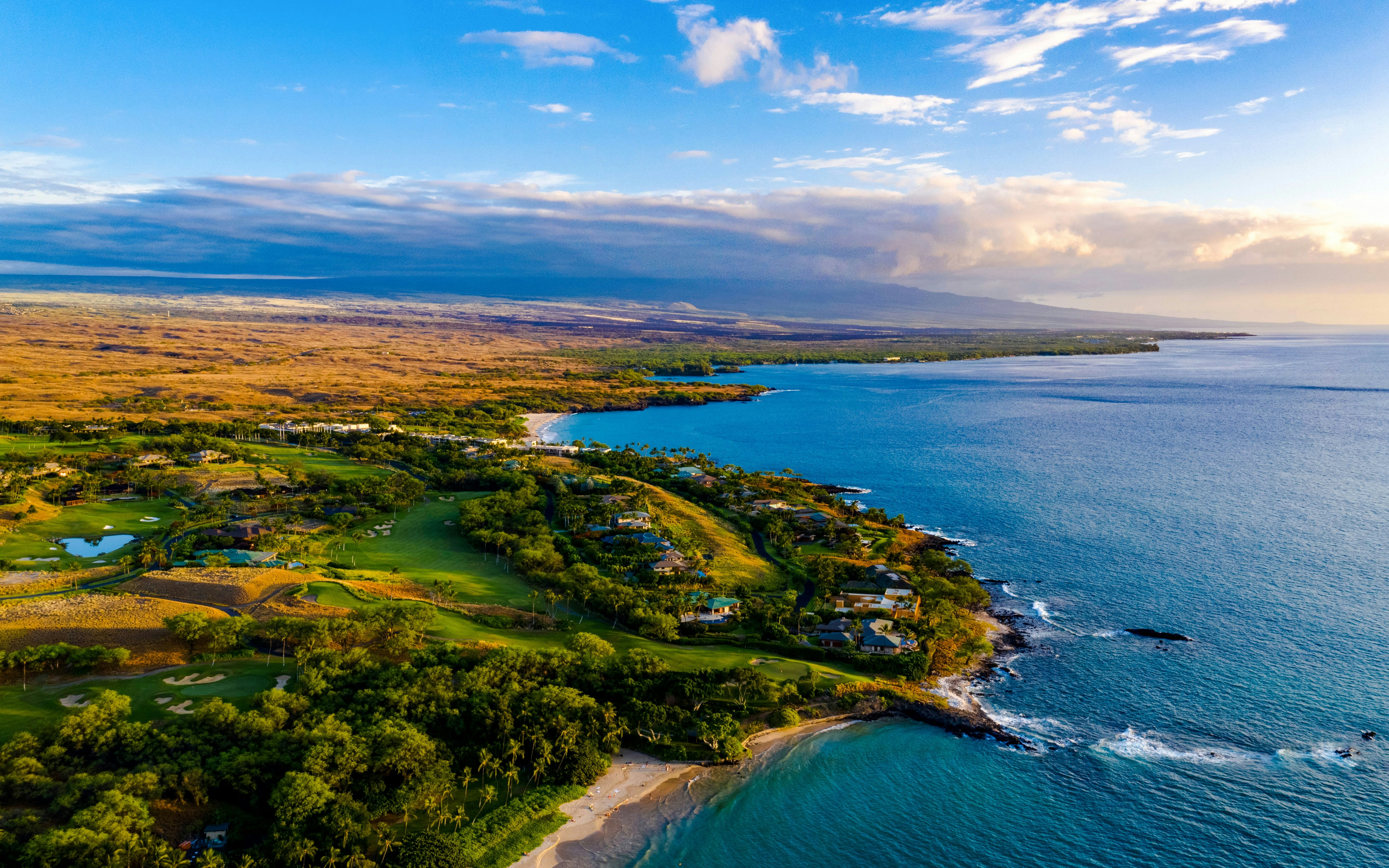 Aerial view of the Kona Coast, Hawaii, featuring lush greenery, sandy beaches, and the Pacific Ocean.