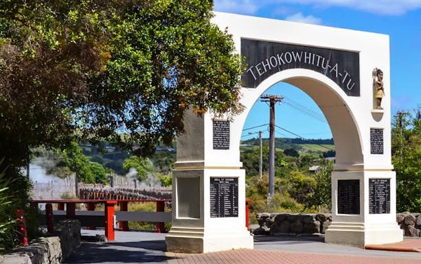 Memorial Archway with inscriptions, surrounded by greenery and distant hills.
