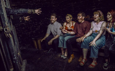 Visitors react to a witch's hands reaching out at York Dungeon's Curse of the Witch experience.
