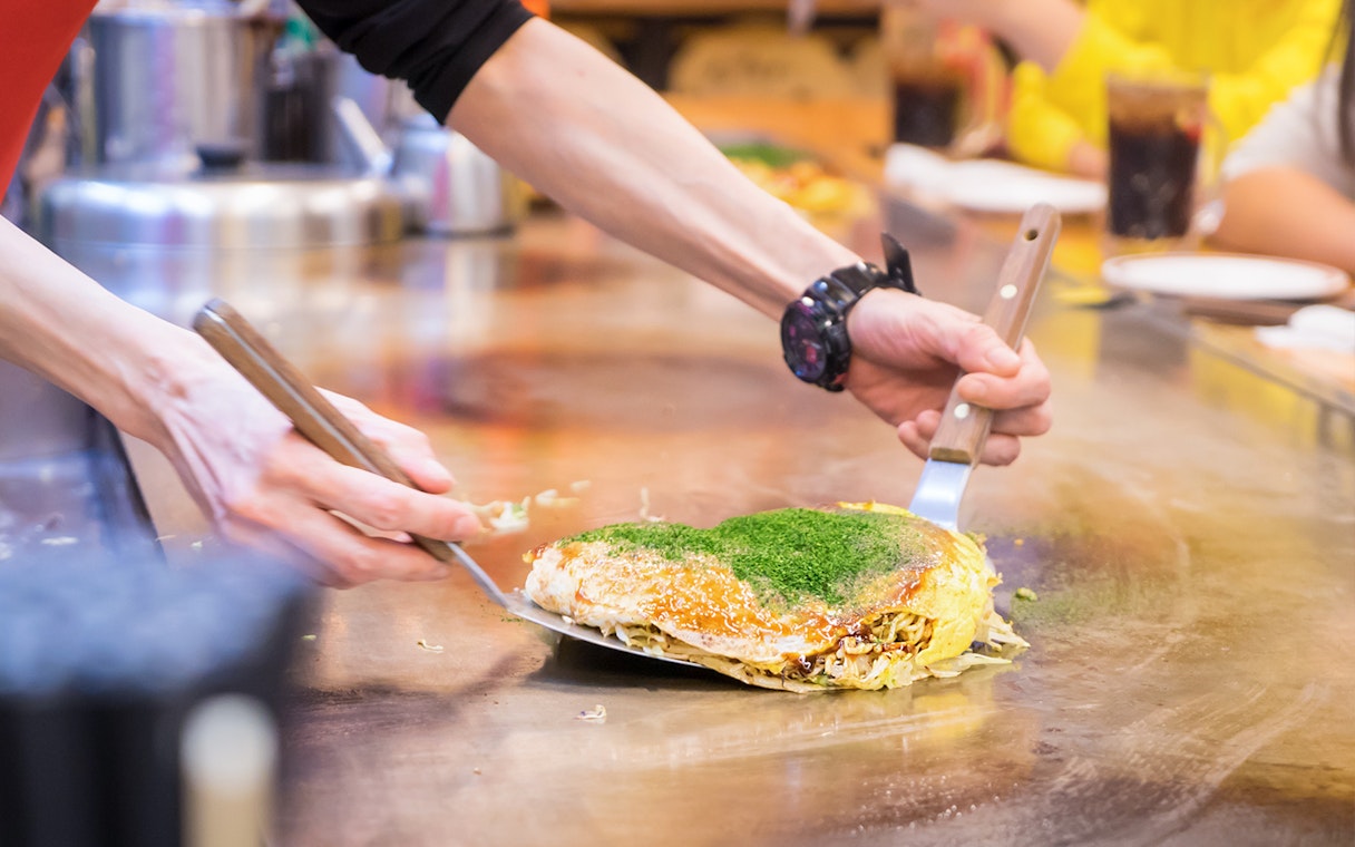 Chef preparing okonomiyaki on a hot griddle in Japan.