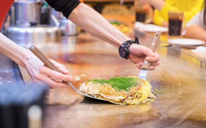 Chef preparing okonomiyaki on a hot griddle in Japan.