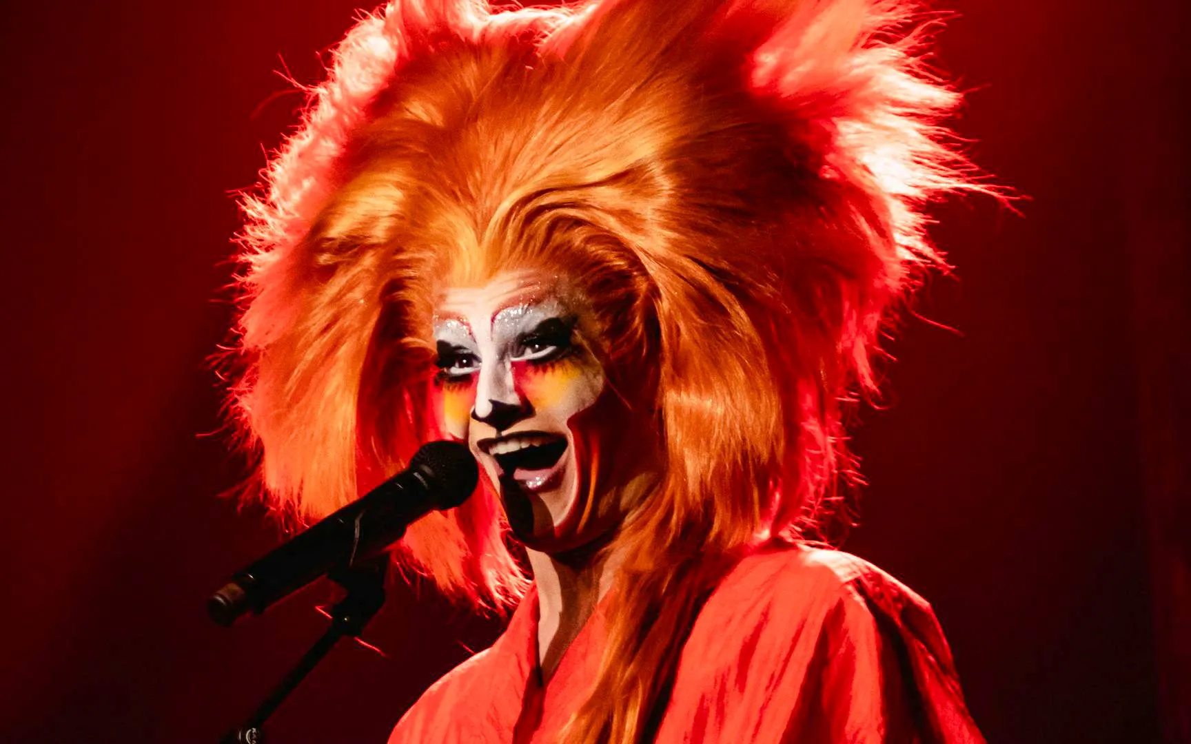Performer with vibrant makeup and wig singing at Madame Arthur cabaret show.