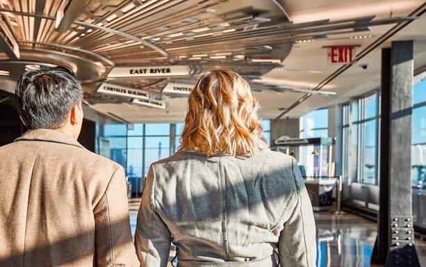 Visitors exploring the Empire State Building's observation deck with directional signs above.