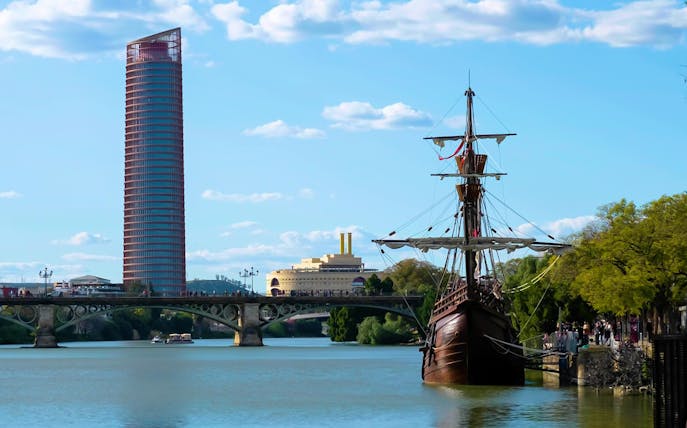Triana Quarter tour with river view, historic ship, and modern tower in Seville.