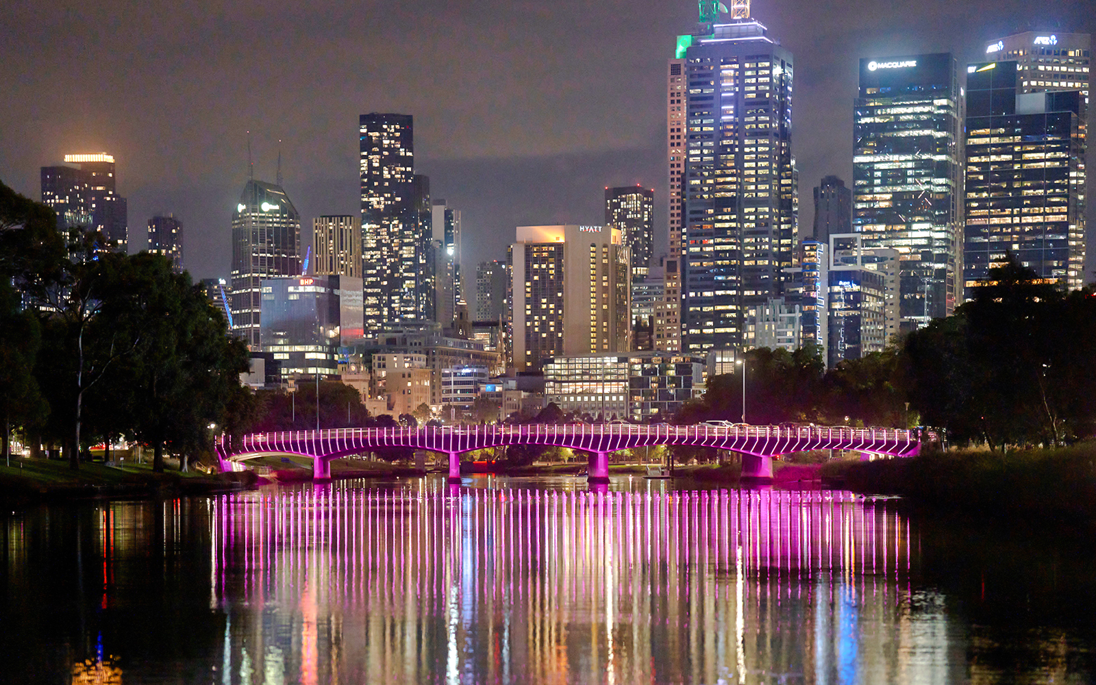 Melbourne city skyline at night with illuminated bridge reflecting on the Yarra River.