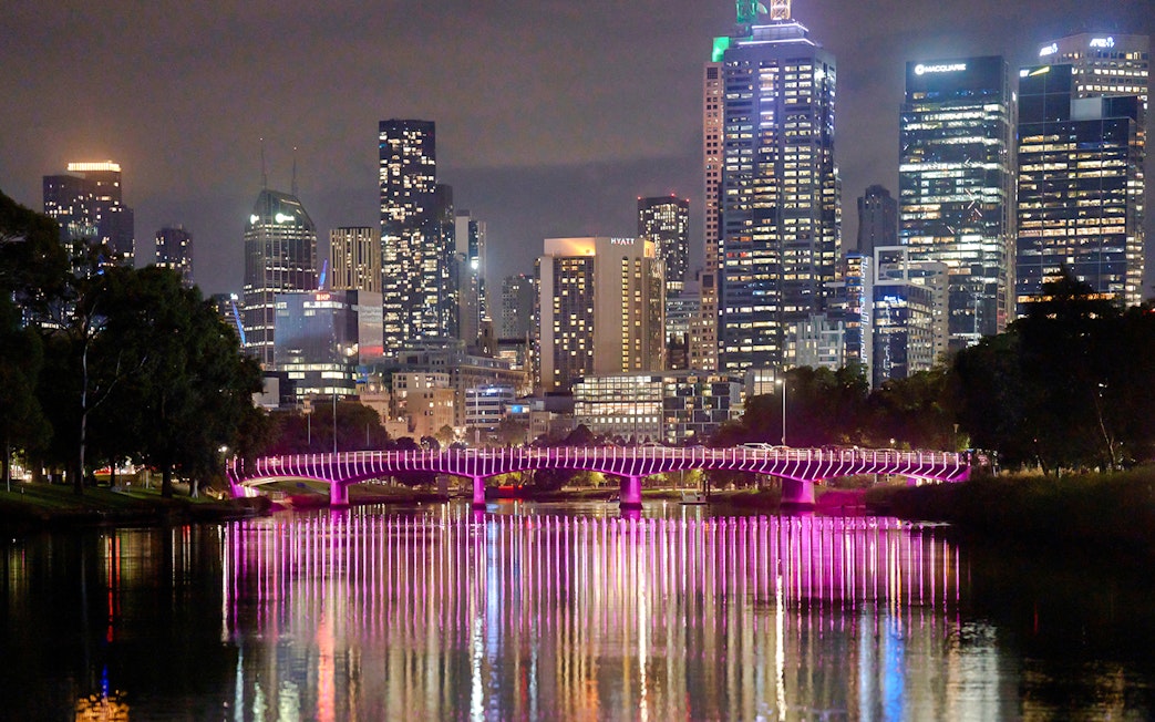 Melbourne city skyline at night with illuminated bridge reflecting on the Yarra River.
