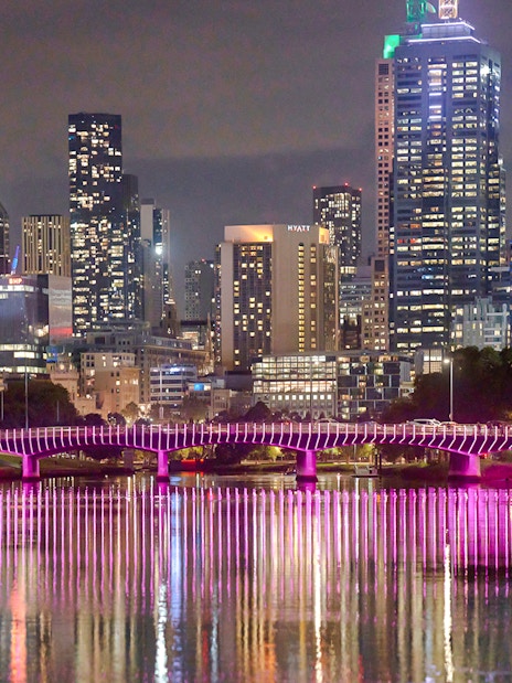 Melbourne city skyline at night with illuminated bridge reflecting on the Yarra River.