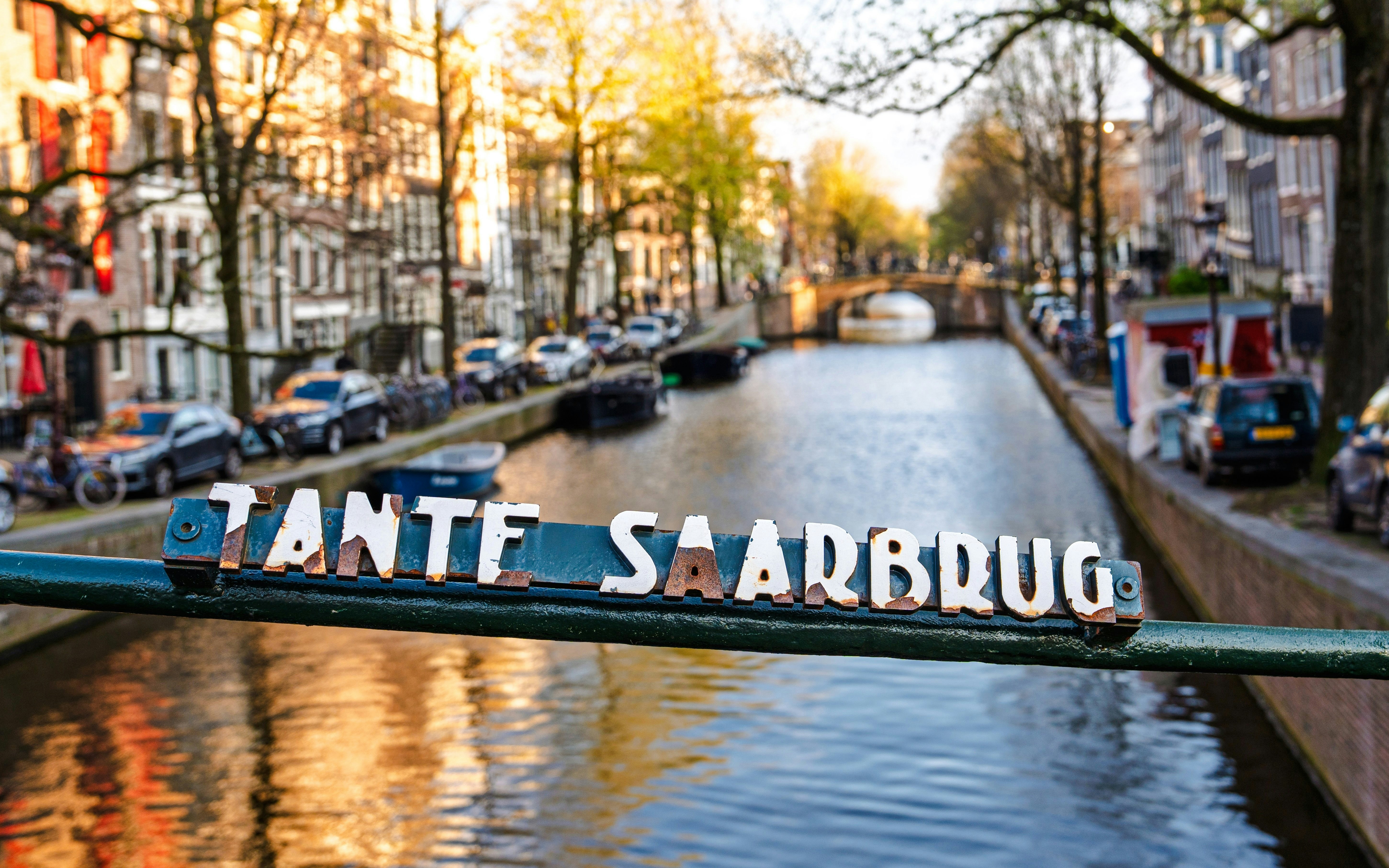 Tante Saarbrug bridge over a canal in Amsterdam with parked cars and trees lining the street.