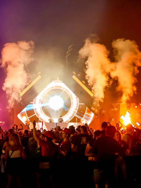 Crowd enjoying a vibrant night concert at Emirates Dubai 7s with colorful lights and smoke effects.