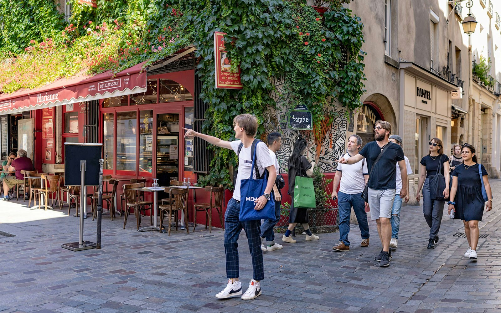 Group exploring Marais neighborhood in Paris, passing a café with ivy-covered walls.