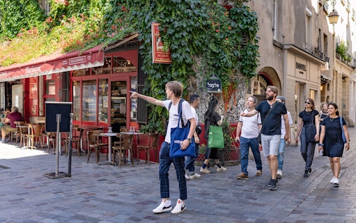 Group exploring Marais neighborhood in Paris, passing a café with ivy-covered walls.