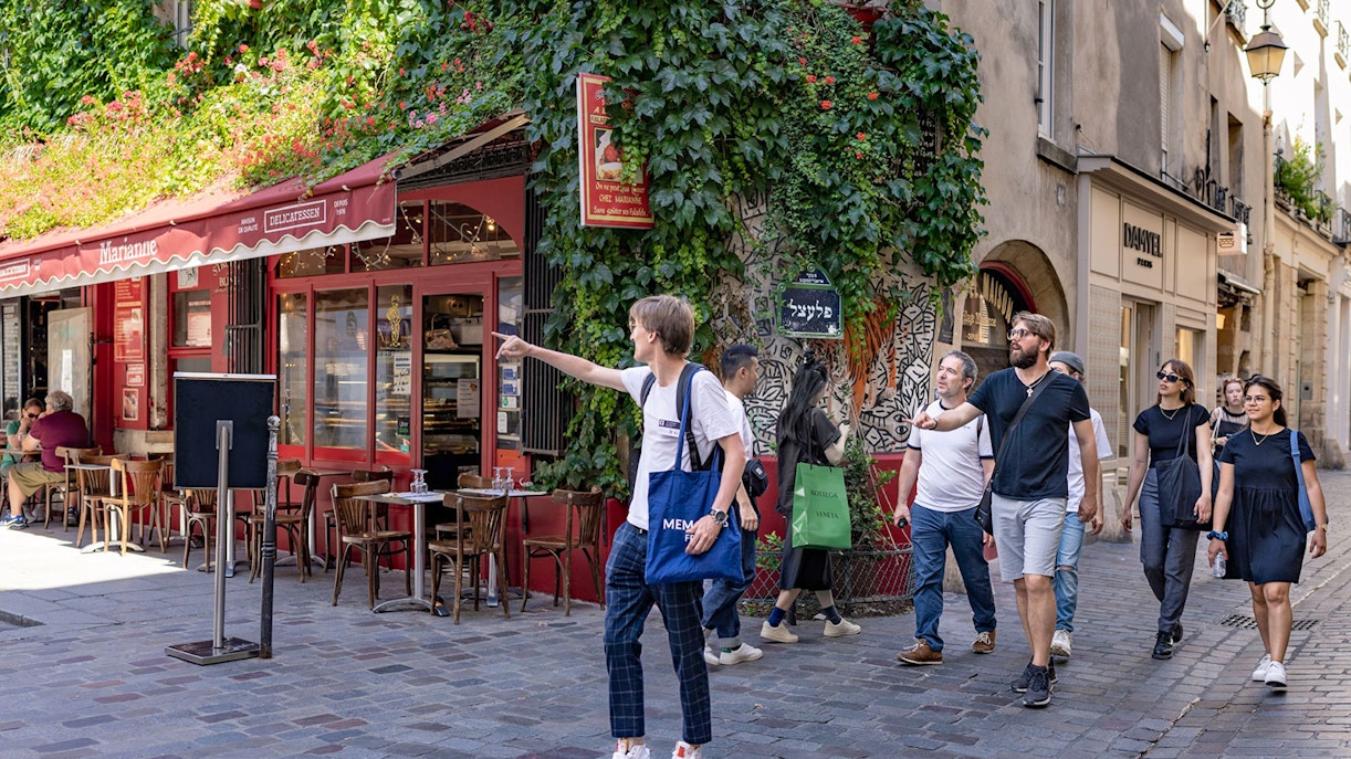 Group exploring Marais neighborhood in Paris, passing a café with ivy-covered walls.