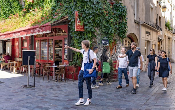 Group exploring Marais neighborhood in Paris, passing a café with ivy-covered walls.