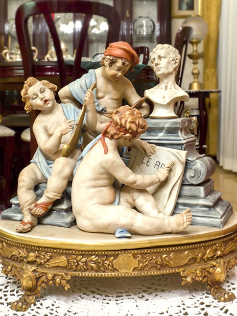 Capodimonte porcelain figurines depicting cherubs with musical instruments and a bust in an ornate room.