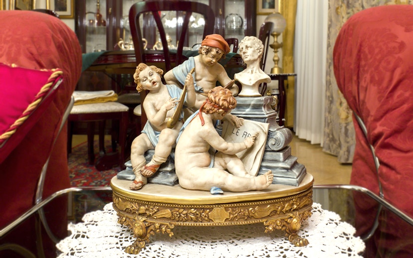 Capodimonte porcelain figurines depicting cherubs with musical instruments and a bust in an ornate room.