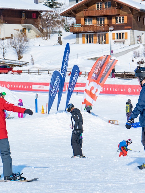 Beginner snowboarders practicing at Grindelwald snow park with chalets in the background.