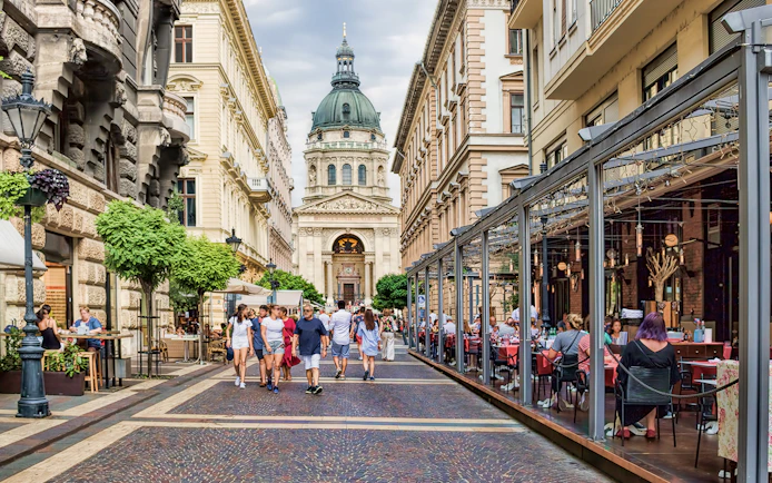 Street view of St. Stephen's Basilica in Budapest with people dining and walking.