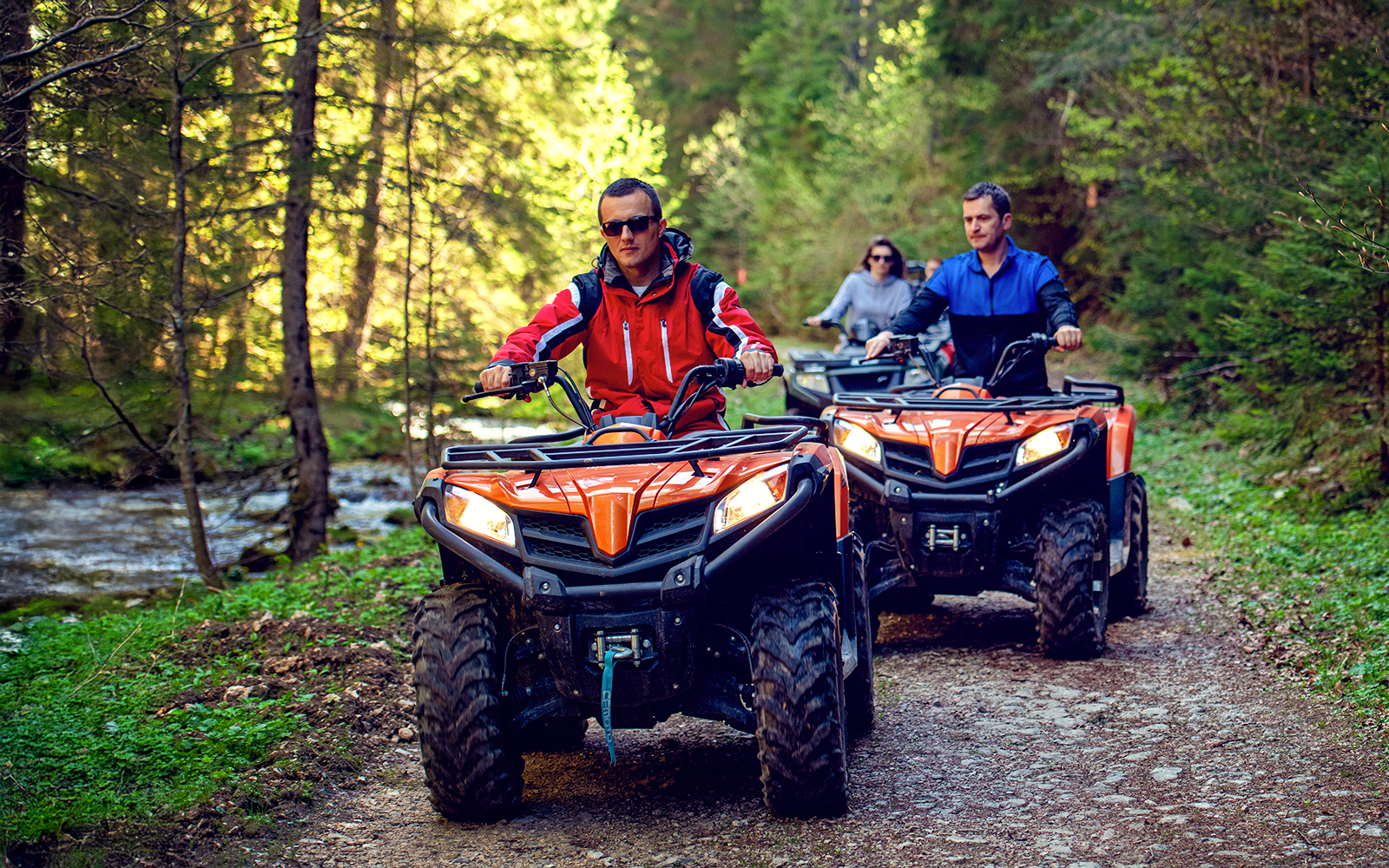 Man riding ATV on forest trail with group following.