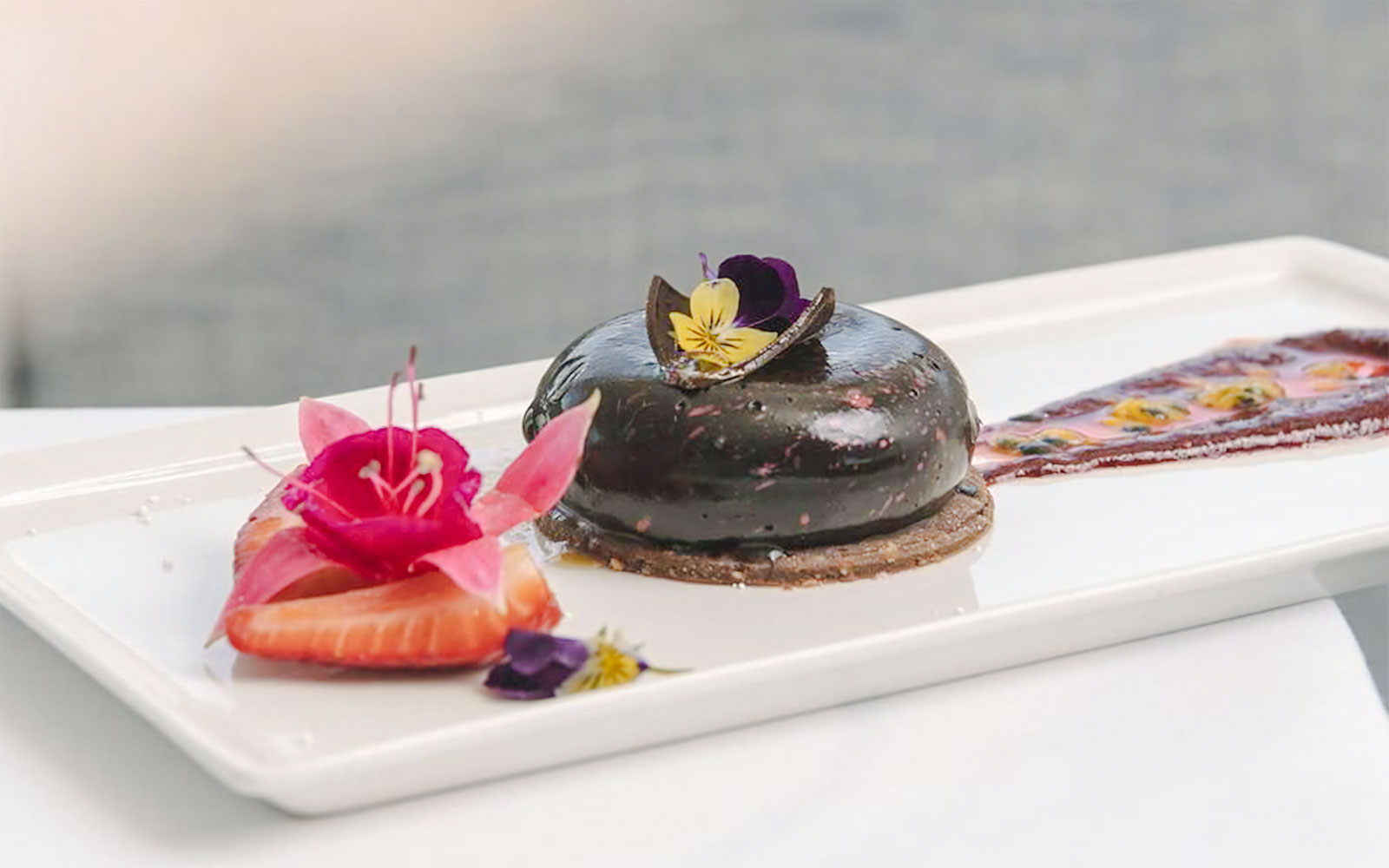 Rich mousse cake with fresh fruit and edible flowers on a white plate.