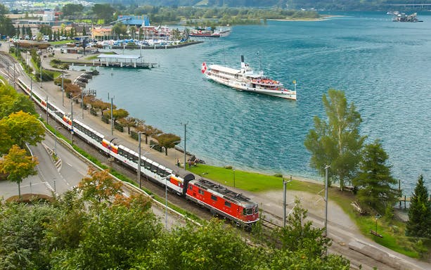 Train and boat on Gotthard Panorama Express route by a lake in Switzerland.