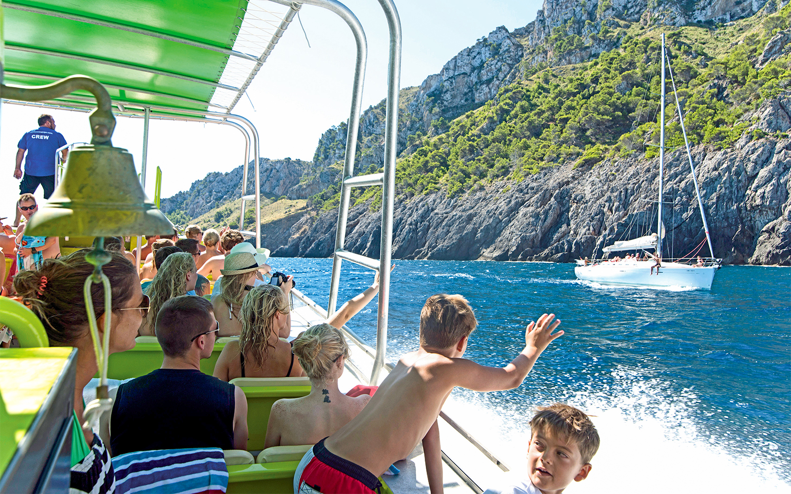 Boat tour in Alcudia with passengers viewing rocky coastline and sailboat nearby.