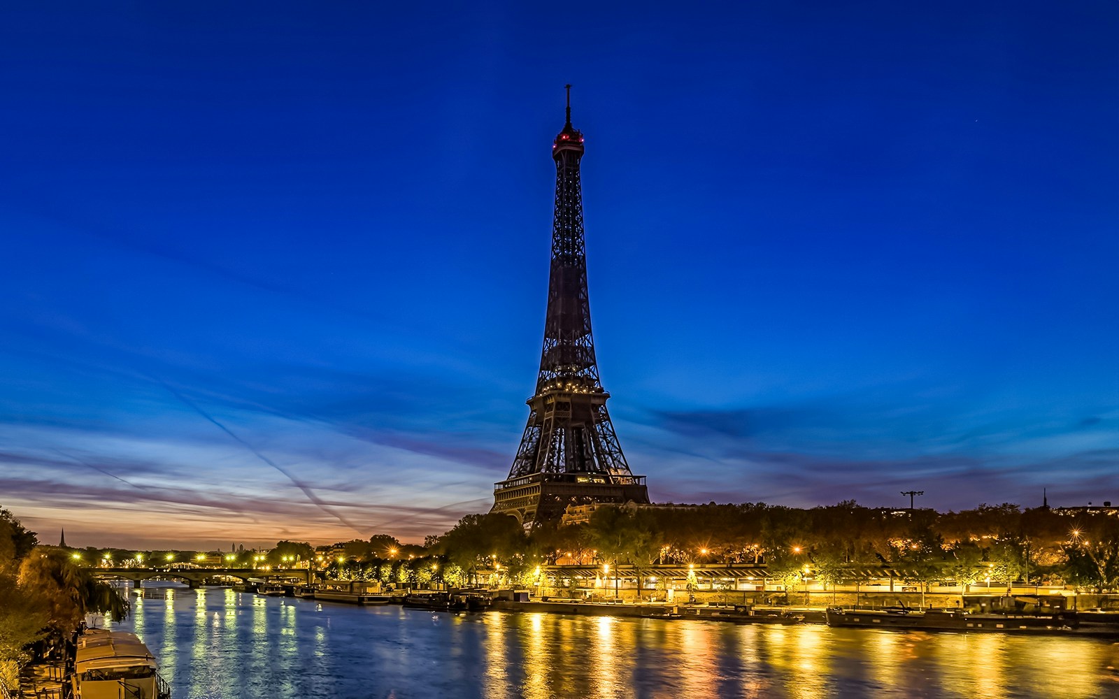 Eiffel Tower illuminated at evening with Seine River in foreground, Paris.