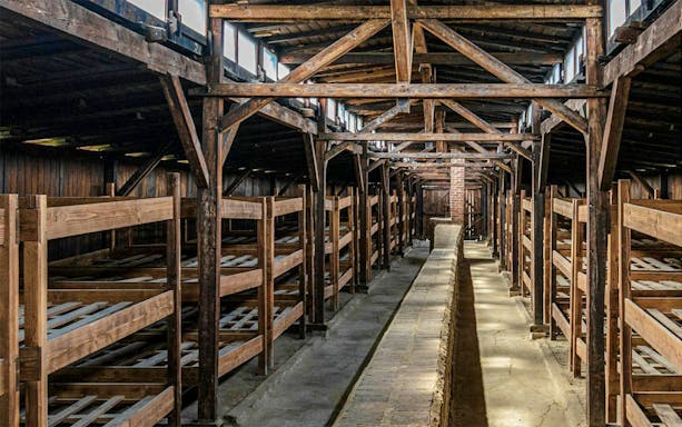 Barracks interior at Auschwitz I, showcasing wooden bunks and structural beams.