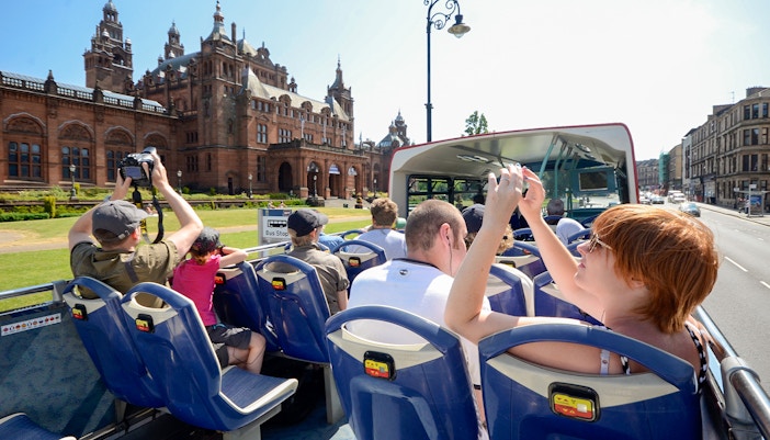 Open-top bus tour passing Kelvingrove Art Gallery in Glasgow.