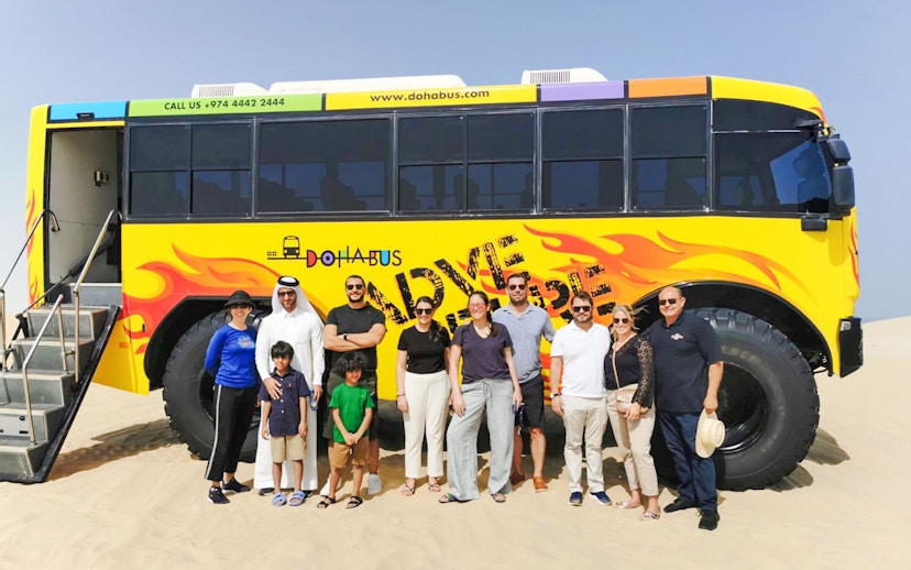 Tourists standing in front of a Monster Bus on a desert tour in Doha.