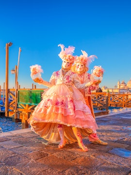 Participants in elaborate costumes at Venice Carnival with St. Mark's Basilica in the background.