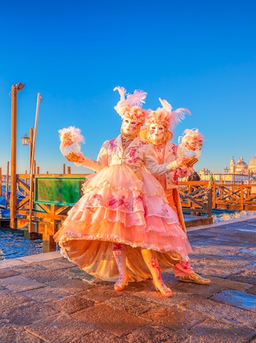 Participants in elaborate costumes at Venice Carnival with St. Mark's Basilica in the background.