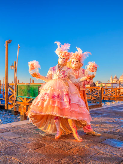 Participants in elaborate costumes at Venice Carnival with St. Mark's Basilica in the background.