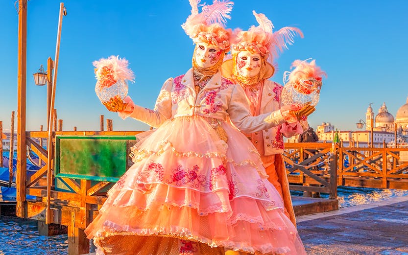 Participants in elaborate costumes at Venice Carnival with St. Mark's Basilica in the background.
