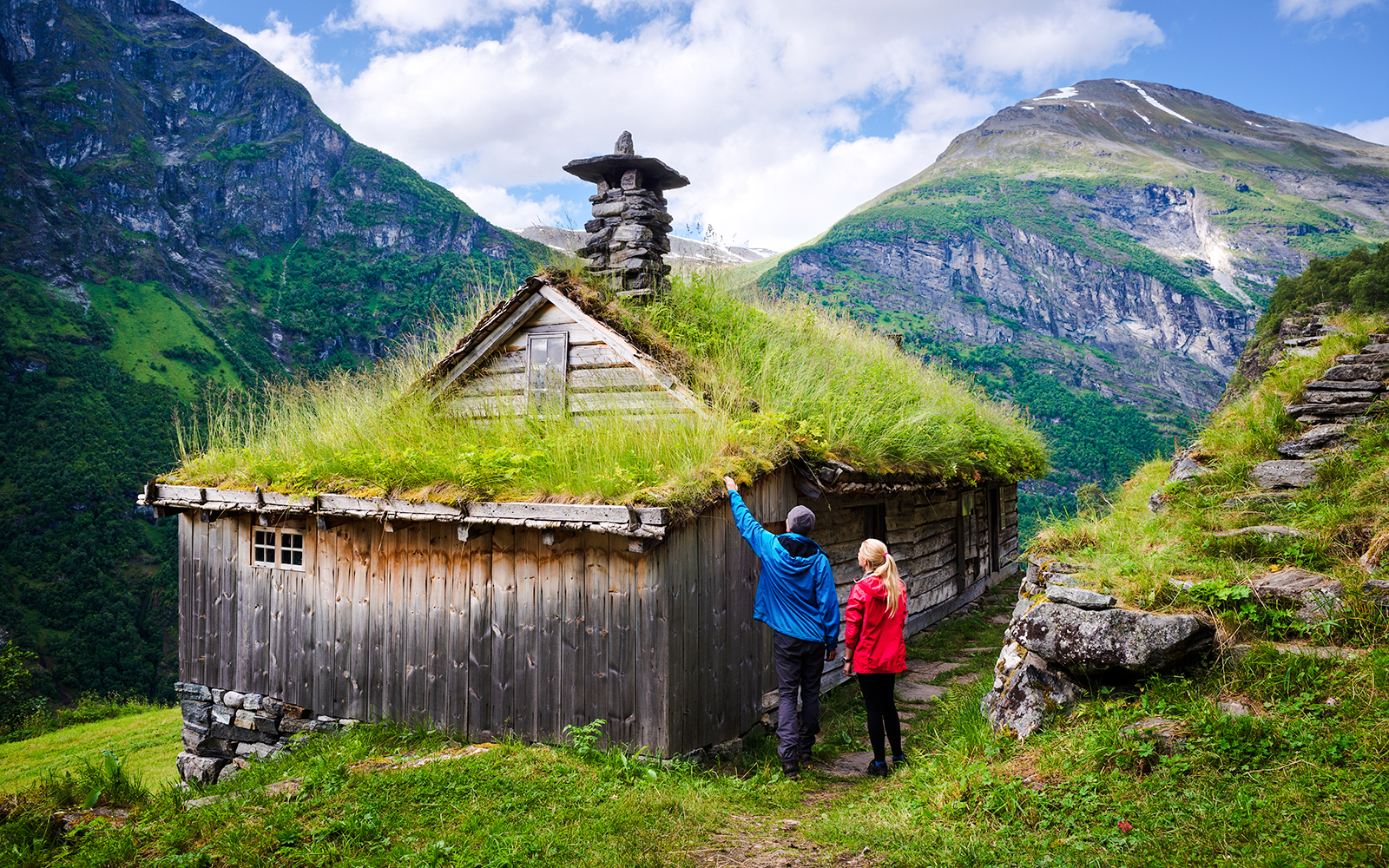 Scandinavian turf house with grass roof near Geiranger fjord, Norway, with two people exploring.