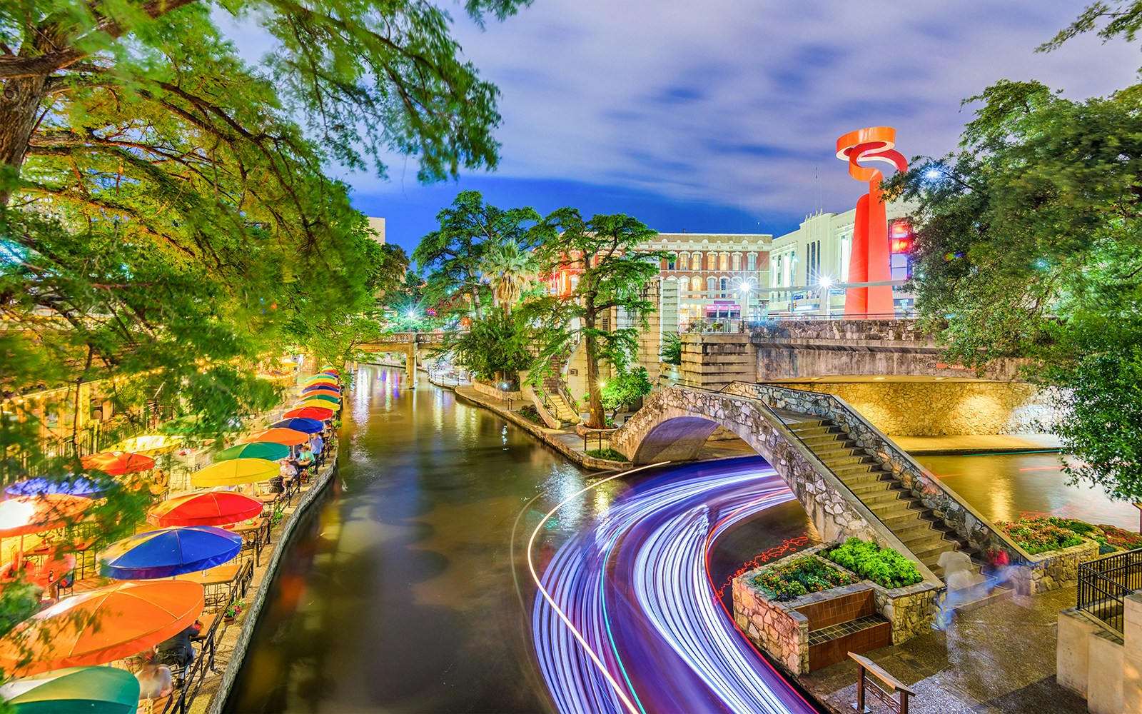San Antonio River Walk with colorful umbrellas and stone bridge at night.