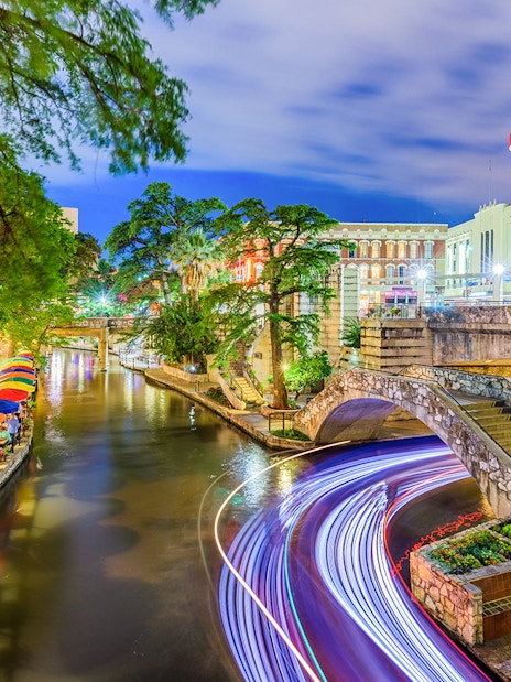 San Antonio River Walk with colorful umbrellas and stone bridge at night.