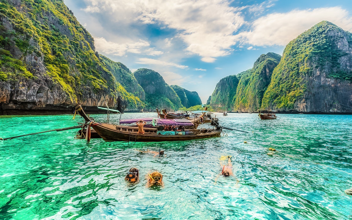 Snorkelers exploring clear waters at Maya Bay, Phi Phi Islands, Thailand with limestone cliffs.