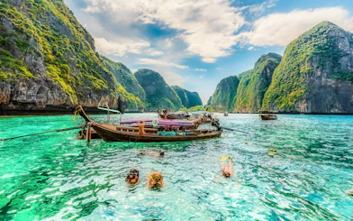 Snorkelers exploring clear waters at Maya Bay, Phi Phi Islands, Thailand with limestone cliffs.