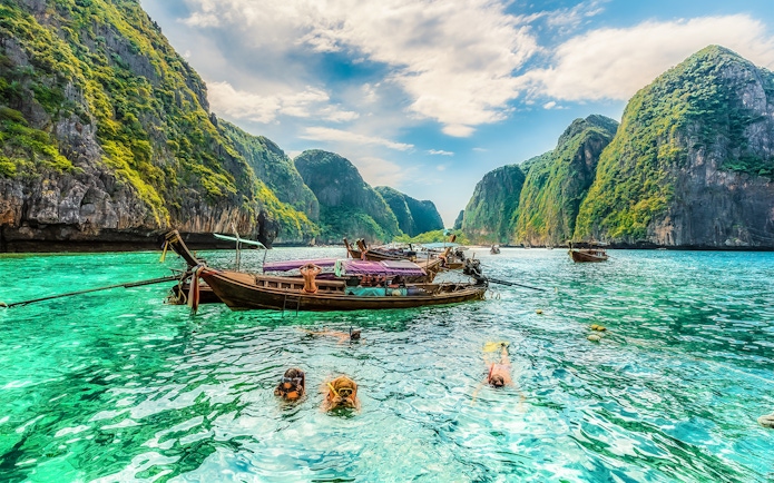 Snorkelers exploring clear waters at Maya Bay, Phi Phi Islands, Thailand with limestone cliffs.