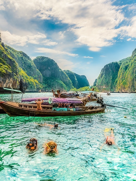 Snorkelers exploring clear waters at Maya Bay, Phi Phi Islands, Thailand with limestone cliffs.