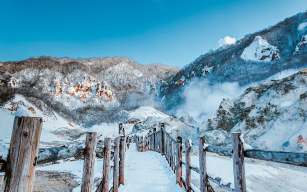 Wooden walkway through snowy Jigokudani Hell Valley, Noboribetsu, Hokkaido, Japan, with steaming vents.