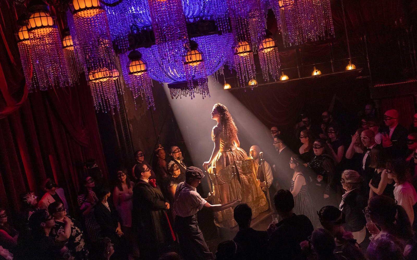 Masquerade Broadway stage performance with actors in masks under chandeliers.