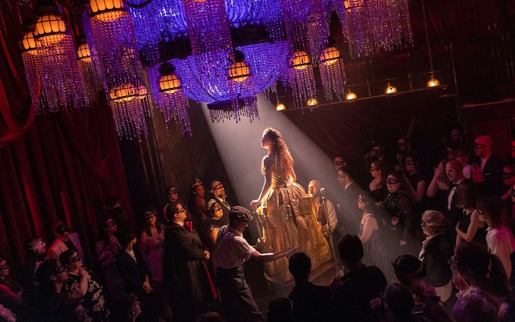 Masquerade Broadway stage performance with actors in masks under chandeliers.