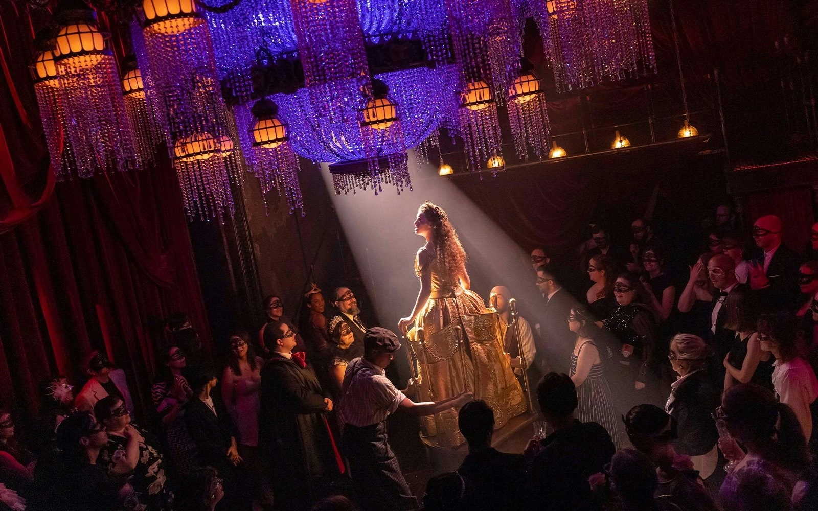 Masquerade Broadway stage performance with actors in masks under chandeliers.