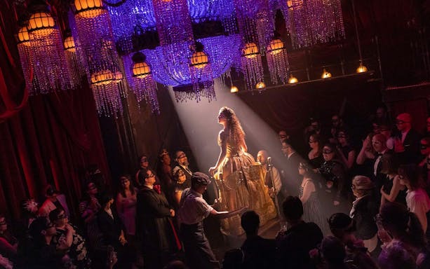 Masquerade Broadway stage performance with actors in masks under chandeliers.