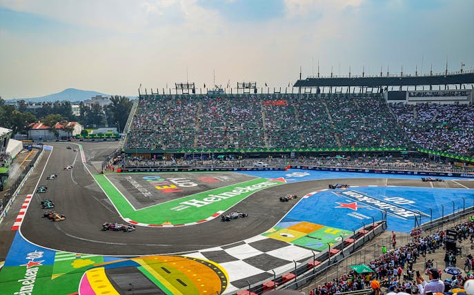 Cars racing on the track at Formula 1 Mexico Grand Prix with a packed stadium.