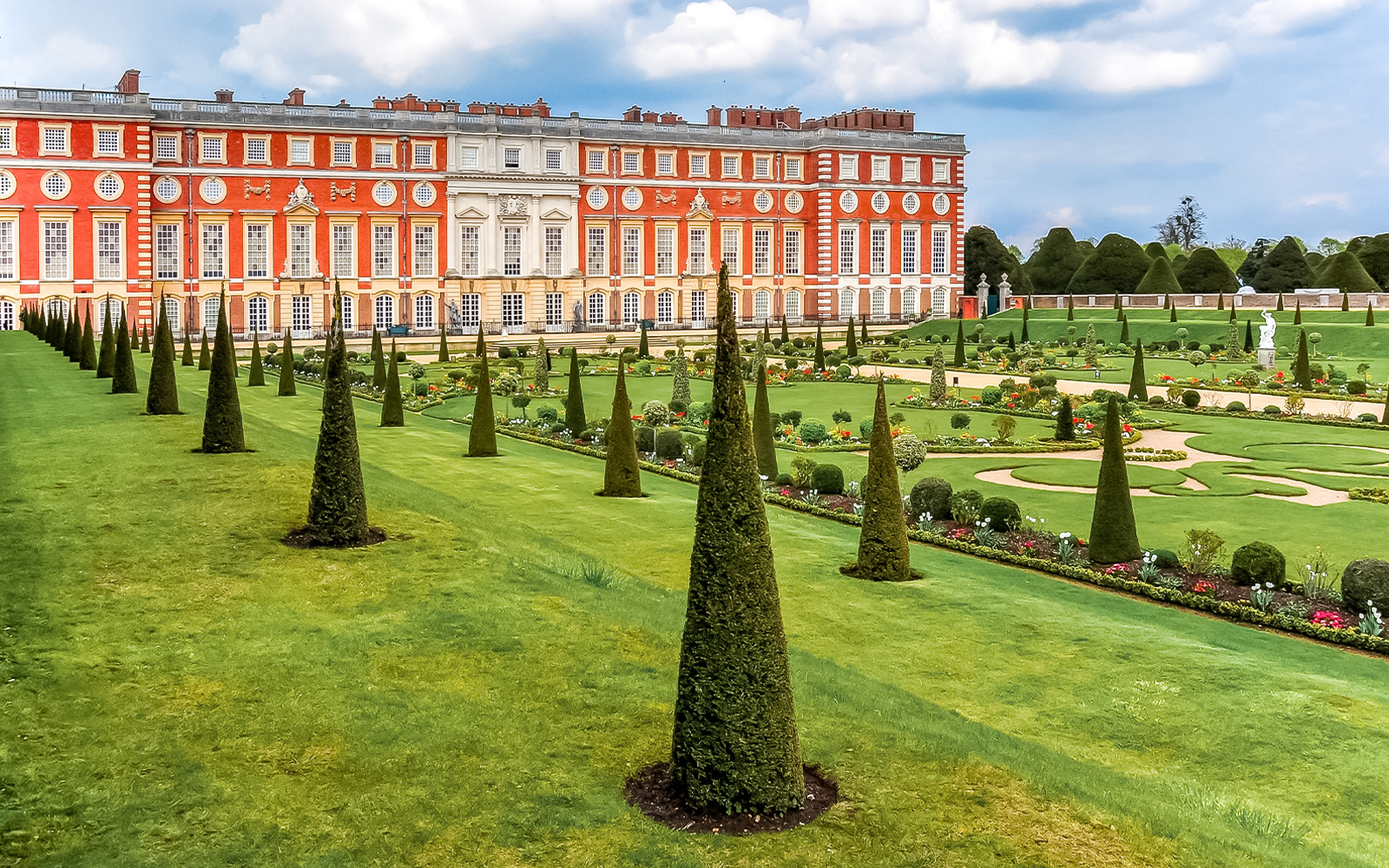 Tourists exploring Privy Gardens at Hampton Court Palace on a sunny day.